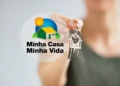 Pessoa segurando as chaves de sua nova casa do programa Minha Casa, Minha Vida, com o logotipo do programa ao fundo.