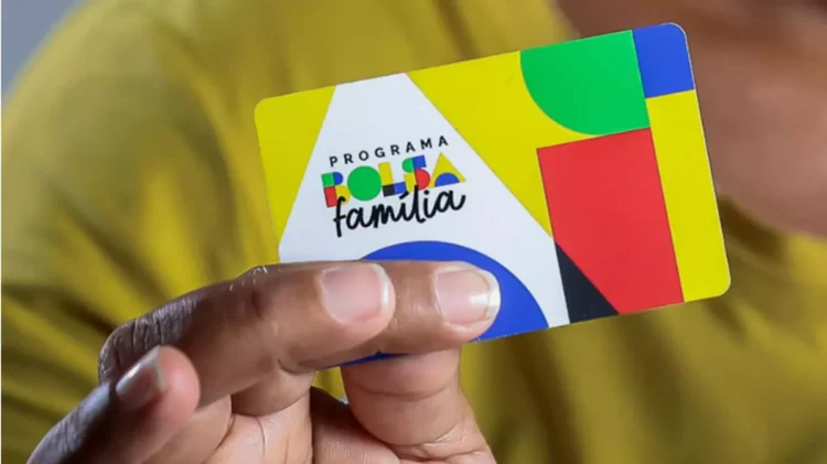 Mão segurando um cartão do Programa Bolsa Família com design colorido.