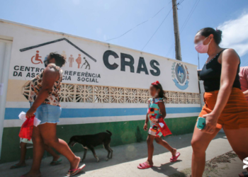 Pessoas caminhando em frente a uma unidade do CRAS sob um dia profundo.