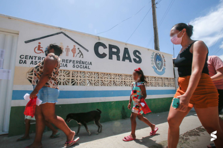 Pessoas caminhando em frente a uma unidade do CRAS sob um dia profundo.