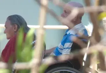"Casal de idosos, um em cadeira de rodas, em ambiente tranquilo, sugerindo cuidado e apoio mútuo.