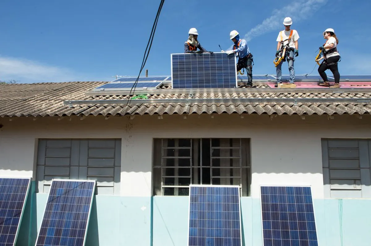 Trabalhadores instalam painéis solares no telhado de uma residência para melhorar a eficiência energética.