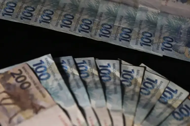 Cédulas de 100 e 200 reais organizadas em leque sobre uma superfície escura.