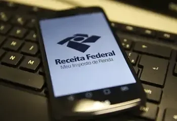 "Smartphone exibindo o logo da Receita Federal com a tela do aplicativo de Imposto de Renda sobre um teclado."