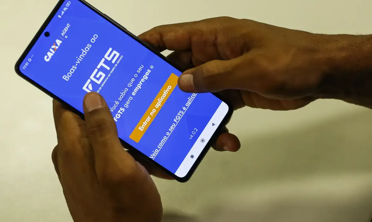 Mãos segurando um smartphone com o aplicativo FGTS aberto na tela.