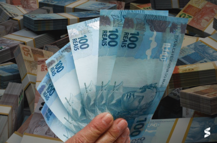 Imagem de cédulas de R$ 100 e R$ 50 empilhadas, com uma mão segurando cédulas de R$ 100, representando a aprovação de pagamento mensal de R$ 2.275 para brasileiros com CPF final 0 a 9.