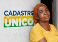 Mulher idosa em frente a parede com logotipo do Cadastro Único, representando beneficiários dos programas sociais em 2025.