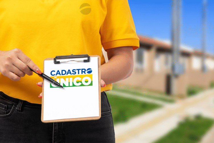 Pessoa segurando uma prancheta com o logo do CadÚnico em frente a um conjunto habitacional.