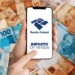 Mãos segurando celular com logotipo da Receita Federal e mensagem sobre Imposto de Renda, com notas de real ao fundo.