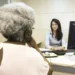 Beneficiária conversa com atendente em agência para resolver pendências de valores do INSS.