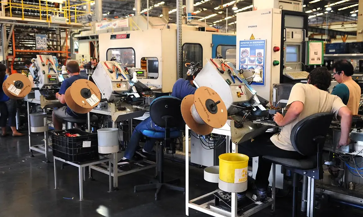 rabalhadores em linha de produção industrial, representando o ambiente de trabalho em dias convocados.