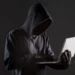 Criminoso escondido nas sombras utilizando um laptop, simbolizando a prática de golpes em compras online.