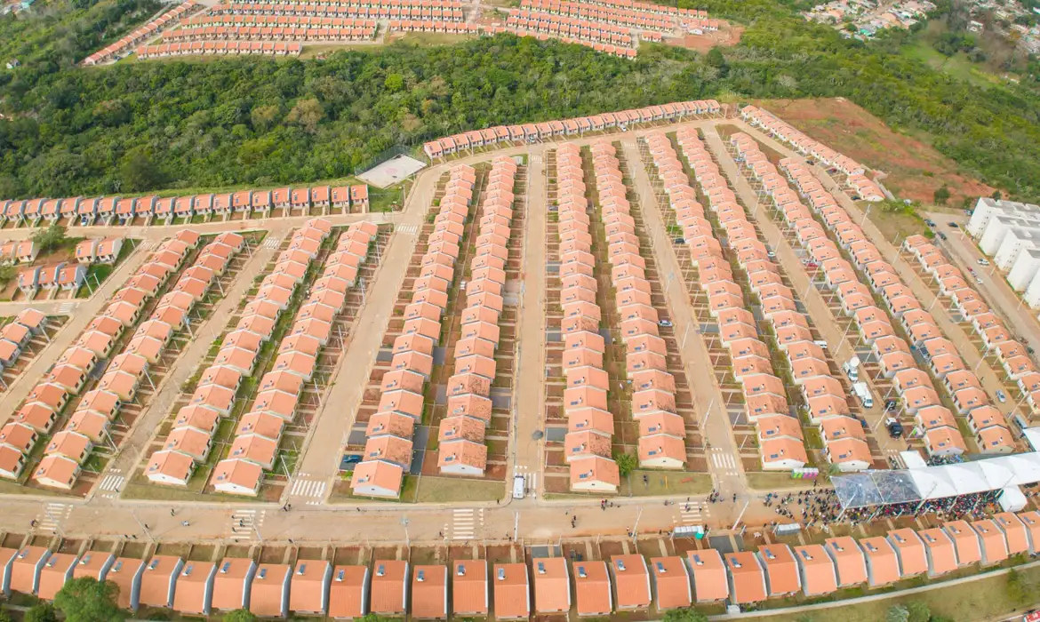 "Vista aérea de um conjunto habitacional com casas de telhado vermelho, mostrando as ruas e áreas organizadas para acomodar muitas famílias."
