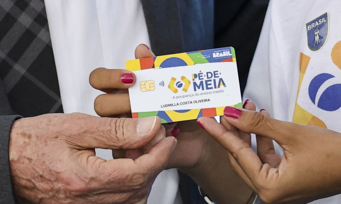 Cartão do Programa Pé-de-Meia sendo segurado por estudante com fundo colorido e logo do programa.