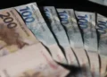 Cédulas de 100 e 200 reais representando o saque de até R$ 2.900, com a imagem de uma mão segurando as notas