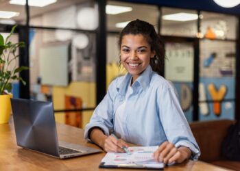 Mulher jovem com laptop e documentos em espaço de trabalho vibrante