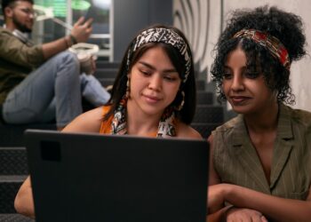 Duas jovens concentradas em um laptop com ambiente moderno ao fundo