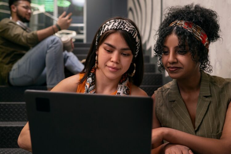 Duas jovens concentradas em um laptop com ambiente moderno ao fundo