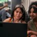 Duas jovens concentradas em um laptop com ambiente moderno ao fundo