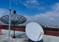 Antenas de satélite em um telhado com vista para a cidade, representando conexão e tecnologia.