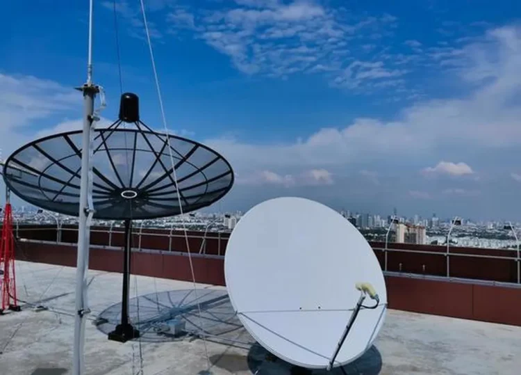 Antenas de satélite em um telhado com vista para a cidade, representando conexão e tecnologia.