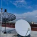 Antenas de satélite em um telhado com vista para a cidade, representando conexão e tecnologia.