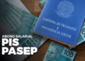 Carteira de trabalho ao lado de cédulas de 100 reais com destaque para o abono salarial PIS/Pasep