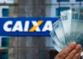 Pessoa segurando cédulas de R$ 100 com o logo da Caixa Econômica ao fundo, representando o uso da Conectividade Social.