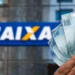 Pessoa segurando cédulas de R$ 100 com o logo da Caixa Econômica ao fundo, representando o uso da Conectividade Social.