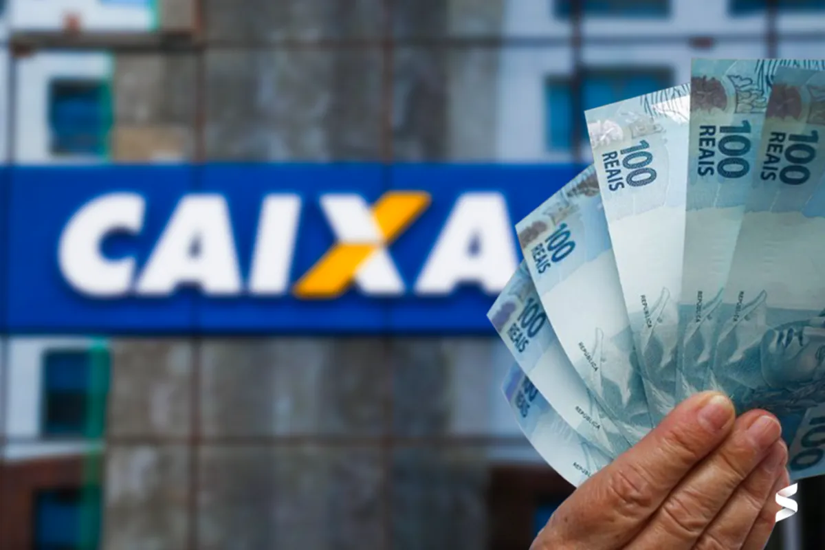 Pessoa segurando notas de 100 reais em frente a uma agência da Caixa Econômica Federal.