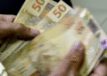 Pessoa contando cédulas de 50 reais, simbolizando o valor de até R$ 6.220 disponível para saque