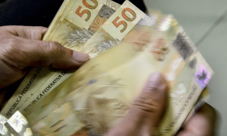 Pessoa contando cédulas de 50 reais, simbolizando o valor de até R$ 6.220 disponível para saque