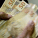 Pessoa contando cédulas de 50 reais, simbolizando o valor de até R$ 6.220 disponível para saque