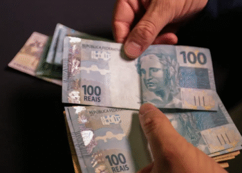 Pessoa contando notas de R$ 100, representando o saque 100% digital de valores acima de R$ 6 mil, disponível para quem atende aos critérios.