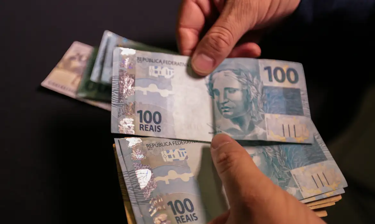 Pessoa retirando cédulas de R$ 100, simbolizando o pagamento do décimo terceiro salário.