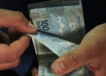 Pessoa segurando cédulas de R$ 100, simbolizando o valor do décimo terceiro salário de um salário mínimo.