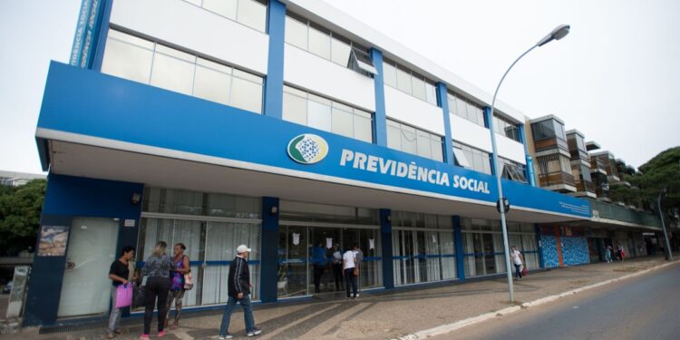 Fachada de agência da Previdência Social com pessoas entrando e saindo.