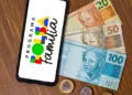 Celular com logo do Programa Bolsa Família ao lado de cédulas e moedas brasileiras