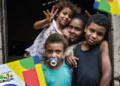 Crianças sorrindo na porta de uma casa, com documentos do Programa Bolsa Família visíveis na imagem.