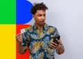 Homem segurando o cartão do Bolsa Família e olhando para o celular em frente a um fundo colorido.