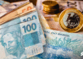 Notas de real e moedas ilustram auxílio de R$ 300 via PIX da Caixa para CPFs selecionados em maio.