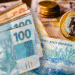 Notas de real e moedas ilustram auxílio de R$ 300 via PIX da Caixa para CPFs selecionados em maio.