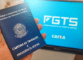 Carteira de Trabalho sendo segurada com tela do FGTS ao fundo, representando a manutenção das regras do saque-aniversário.