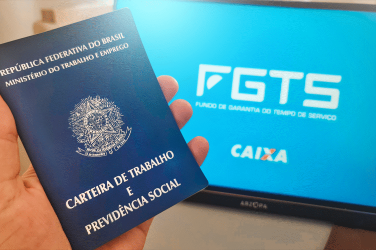 Carteira de Trabalho sendo segurada com tela do FGTS ao fundo, representando a manutenção das regras do saque-aniversário.
