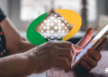 Mão de um idoso segurando um smartphone, com o logo do INSS sobreposto na imagem.