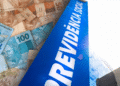 Notas de reais ao lado de fachada do prédio da Previdência Social com o céu ao fundo