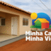 Casa popular recém-construída com rua de terra vermelha e céu nublado.