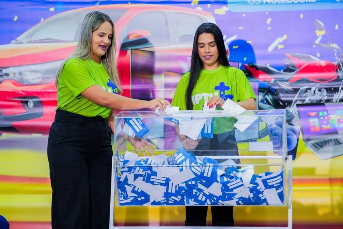 Pessoas participando do sorteio do IPTU Premiado 2025, com cupons sendo sorteados ao fundo.
