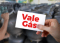 Cartão do Vale Gás sendo segurado por uma mão em frente a botijões de gás