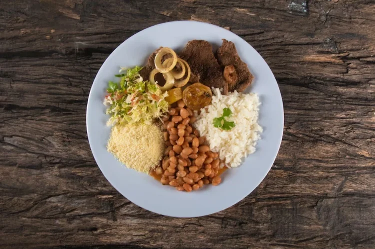Prato tradicional brasileiro com arroz, feijão, carne, salada e farofa, representando alimentação acessível na comunidade.